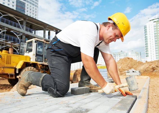 Mason worker bent over concrete, with a yellow hard hat and mallet